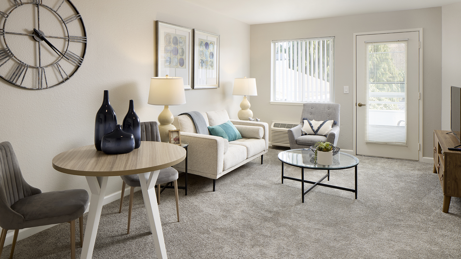 A bright and neatly furnished Holiday Bellevue Garden apartment living room with a cohesive color scheme, featuring a comfortable sofa, an armchair, a round coffee table, and decorative accents.