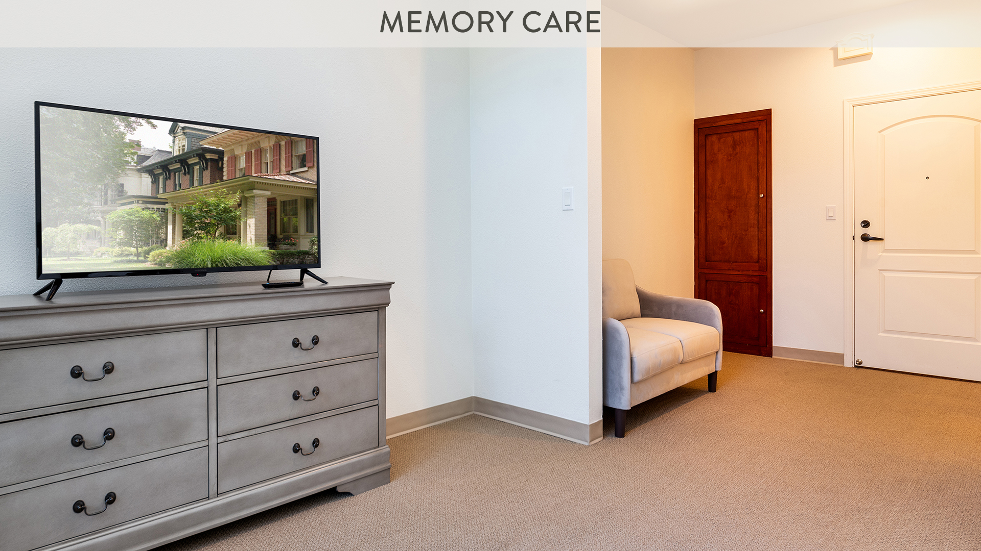 Memory care apartment living room with TV on a chest of drawers and a seating area in front of the door