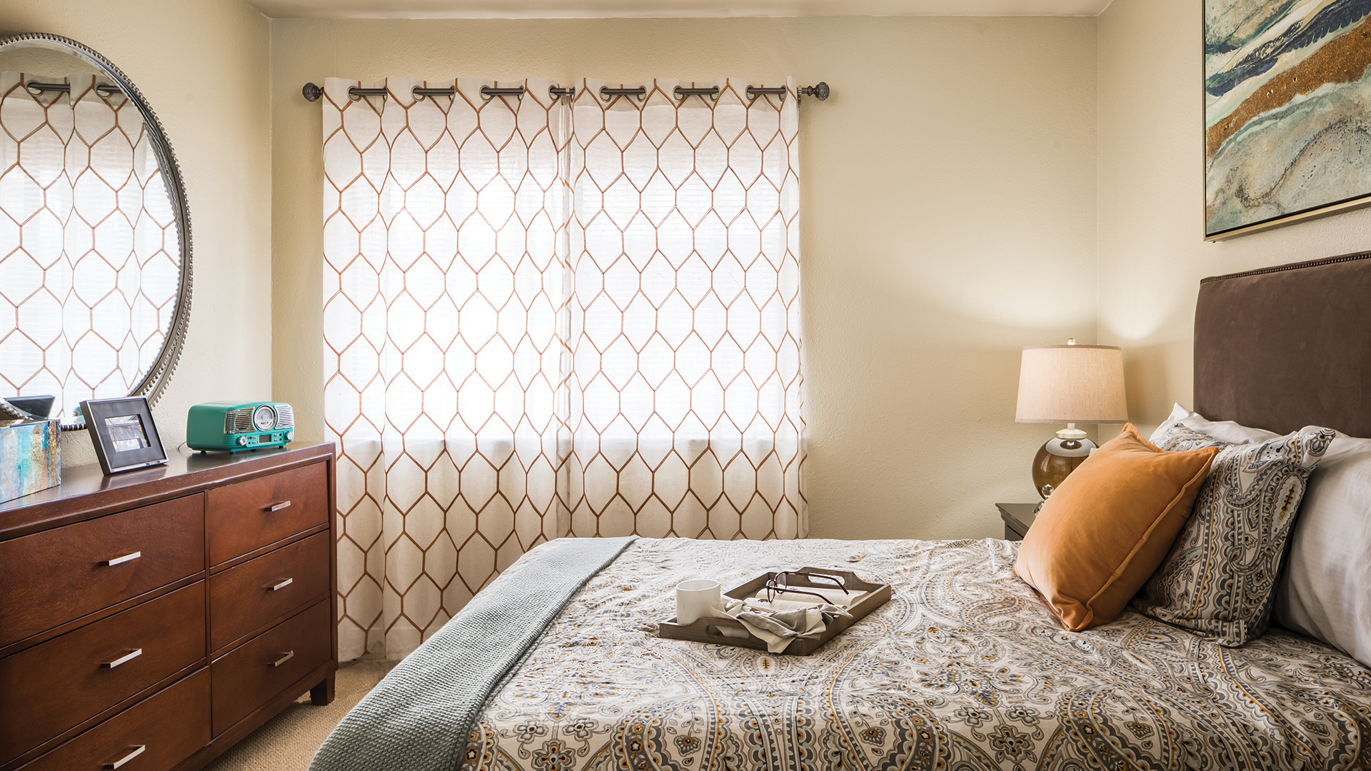 Apartment bedroom with queen bed, dresser, and large window