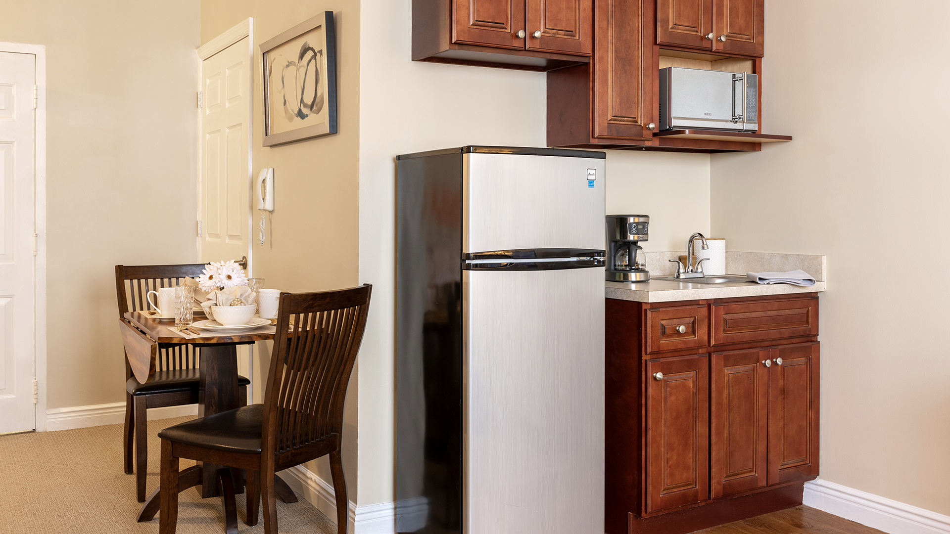 Atria Cranford apartment kitchenette with small refrigerator, microwave, cabinets, and small table and chairs set.
