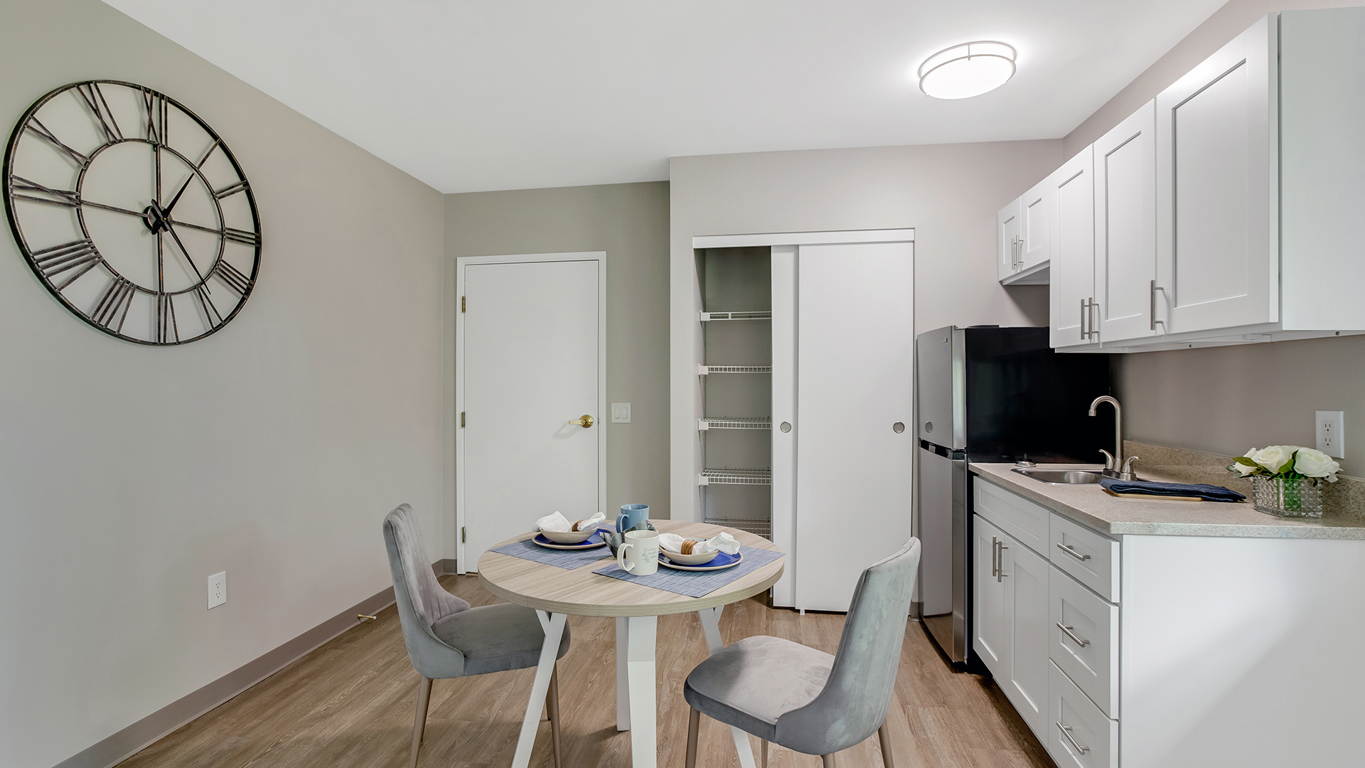 apartment kitchenette model at with small stainless steel refrigerator, counter top space, and two seated table