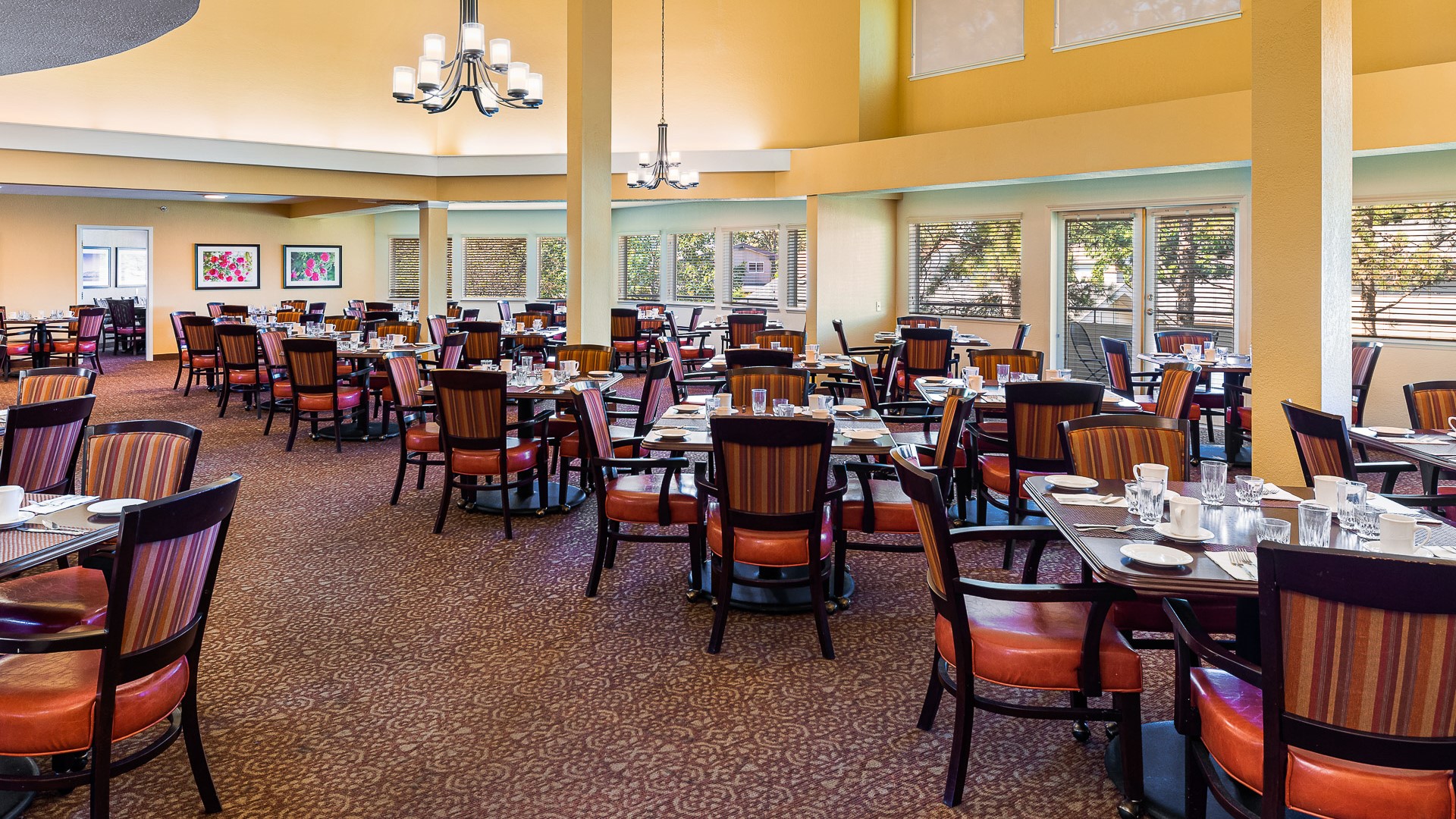 Spacious dining room with neatly set tables, striped chairs, and large windows allowing natural light to brighten the space