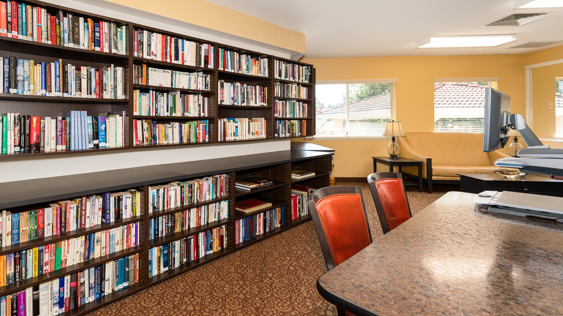 Bright library with full bookshelves, red chairs, and a cozy seating nook by the windows
